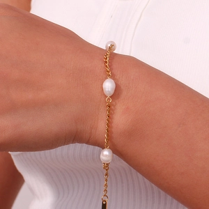 Close-up of gold stainless steel Cuban chain bracelet with three pearls on a female wrist