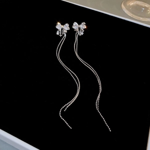 Détail macro des boucles d'oreilles nœud papillon argentées avec pampilles sur fond noir uni