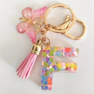 Detailed view of pink resin letter F keychain with sequins, butterfly and suede tassel