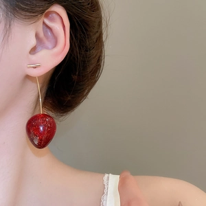 Gros plan d'une boucle d'oreille cerise avec paillettes et clou en barre dorée