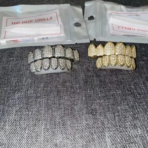 Detailed view of gold and silver hip hop grillz set with tweezers and packaging