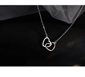 Close-up of interlocking heart pendants on a silver chain against black fabric