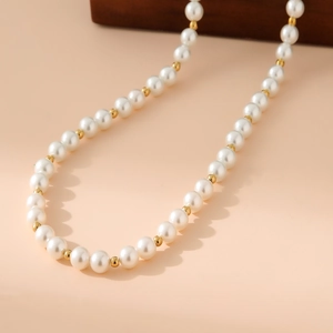 Detailed close-up of white pearls and golden stainless steel beads on a layered necklace
