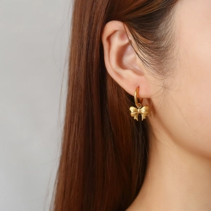 Close-up of a woman wearing gold bow pendant hoop earrings in stainless steel