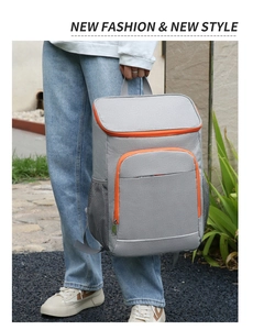 Close-up of gray insulated backpack with orange zippers held by model in outdoor setting