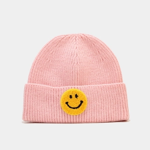 Détail d'un bonnet en maille rose avec écusson smiley jaune et texture côtelée