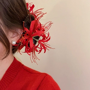 Detailed close-up of a red spider lily hair clip styled on a model's hair with pearls