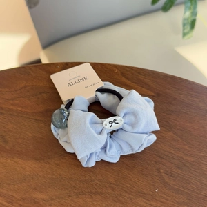 Light blue linen bow hair scrunchie with a decorative bead and brand tag on wood background