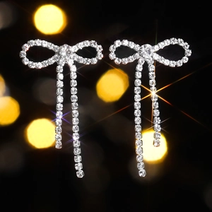 Sparkling silver bow knot tassel earrings with rhinestones on a bokeh background