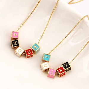 Golden chain necklaces with colorful enamel letter beads spelling AMOUR and LUCKY on white tray