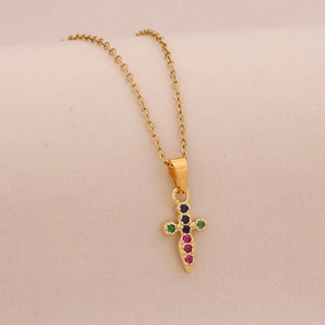 Macro detail of gold cross pendant featuring colorful embedded gems on a fine link chain