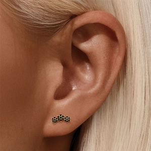 Detailed close-up of a gold stud earring featuring black clusters on a model's ear