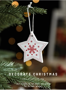 Detail of white wooden star ornament with red snowflake hanging on a Christmas tree branch