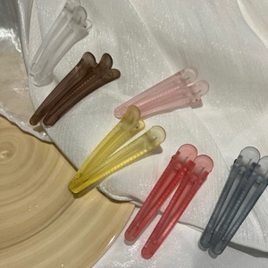Macro shot of matte colorful plastic duckbill hair clips on soft white textured fabric