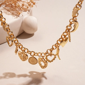 Macro detail of gold chunky chain necklace with heart, moon, and wing charm pendants