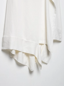 Detail view of white asymmetric dress showing layered hem structure and woven texture