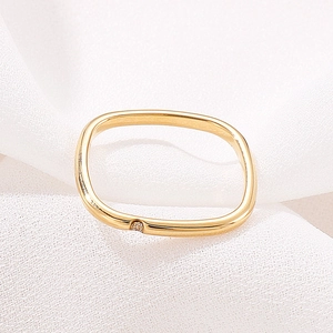 Detailed close-up of a square gold ring featuring a single diamond on white fabric