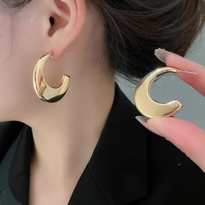 Detail of chunky gold-plated C-shape hoop earrings with a high-shine mirror finish