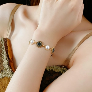 Close-up of vintage gold bracelet with white pearls and black sunflower jewels on wrist
