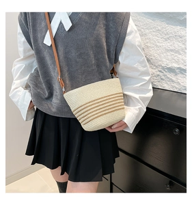 Detailed view of beige straw bucket bag with brown stripes worn by a model