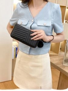 Close-up of black chevron quilted long wallet with pompom charm held by a model
