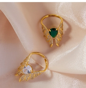 Close-up of gold angel wing rings with green and white drop zircon on beige silk fabric