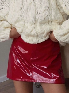Detailed close-up of red glossy faux leather skirt paired with white cable knit sweater