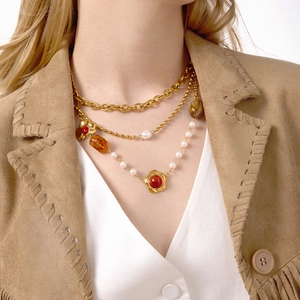 Layered gold necklace with resin pendants and white pearls on a stylish brown fringe jacket