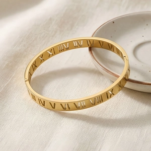 Detail shot of golden Roman numeral cut-out bangle on elegant white textured fabric