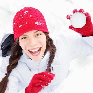 Close-up of a person wearing a bright red winter knit hat and matching gloves in the snow