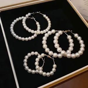 Three pairs of elegant white pearl hoop earrings in different sizes on black velvet