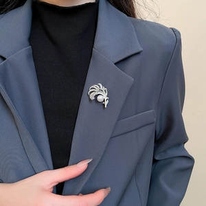 Dettaglio di una spilla a piuma argentata con zirconi e perla su un blazer blu scuro