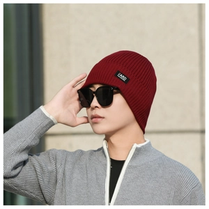Macro view of burgundy ribbed knit beanie showing thick texture and decorative side label