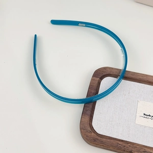 Détail d'un serre-tête bleu en acétate avec de petites dents antidérapantes sur blanc