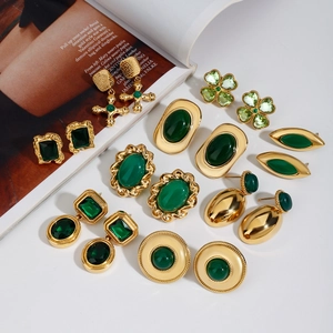 Boucles d'oreilles luxe en acier doré avec pierres vertes sur fond de magazine de mode