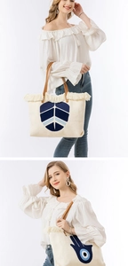 Detail of bohemian canvas tote bag featuring blue embroidery, fringe, and brown leather handles