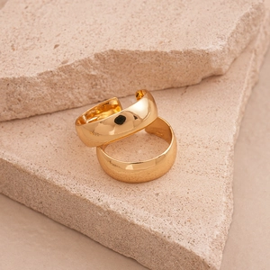 Close-up of two polished gold geometric rings displayed on natural beige stone