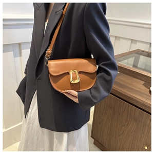 Detail of a brown leather saddle bag featuring a gold horseshoe buckle and adjustable strap