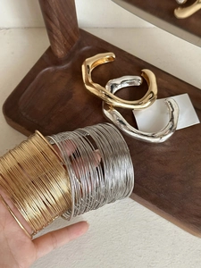 Irregular wide golden cuff and thin metal bangles displayed on a wooden tray
