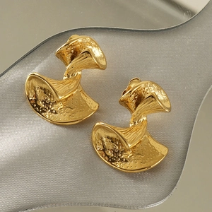 Detailed view of golden hammered texture bow earrings on a grey textured background
