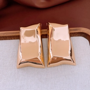 Detailed macro view of gold-tone rectangular earrings with a liquid metal texture