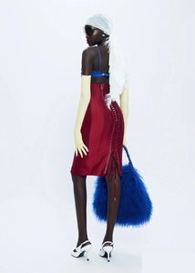 Détail de la jupe en satin rouge avec œillets et grand sac à main en peluche bleue
