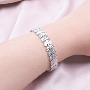 Macro shot of silver C-shaped leaf bracelet with detailed engravings on pink silk