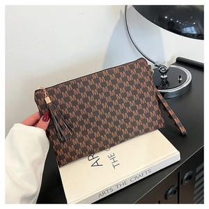 Close-up of brown M-pattern envelope clutch with gold zipper and tassel detail