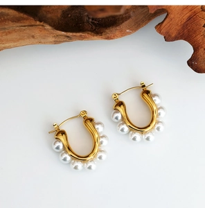 Detailed view of U-shaped gold earrings with embedded pearls on a textured wood background