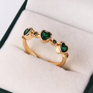 Close-up of gold ring with three heart-shaped green emerald stones on beige velvet