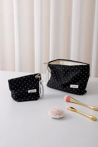 Detailed macro of black polka dot cosmetic bags featuring pearl zipper pull and brand tag