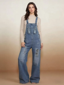 Dettaglio della salopette in denim strappato con fibbie in metallo e trama vintage usurata