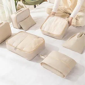 Beige 7-piece travel organizer set with mesh bags and drawstring pouches on a white bed
