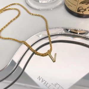 Détail d'un collier doré avec pendentif lettre V serti de zircons brillants et fins
